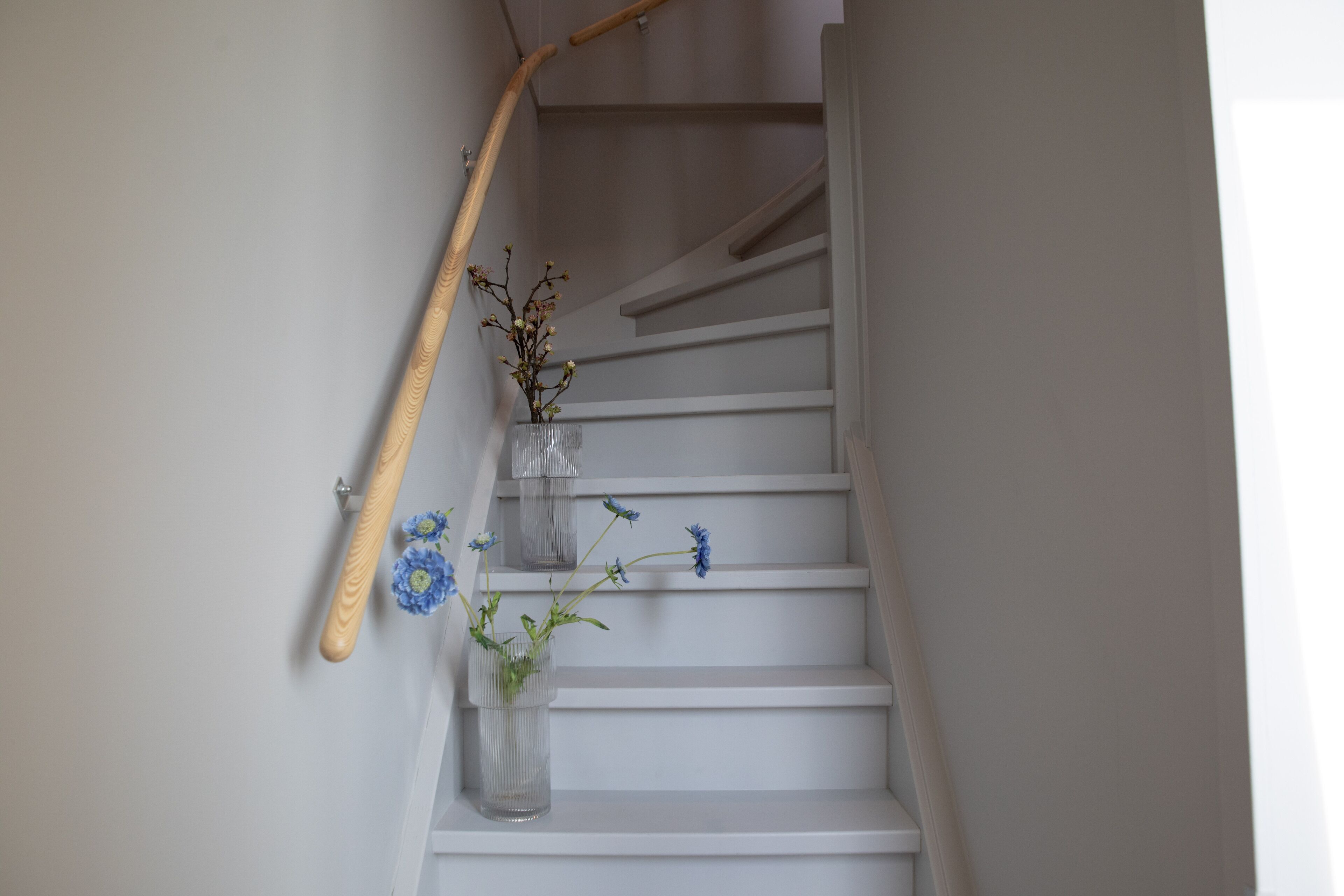 A staircase with a wooden handrail and a vase with flowers.