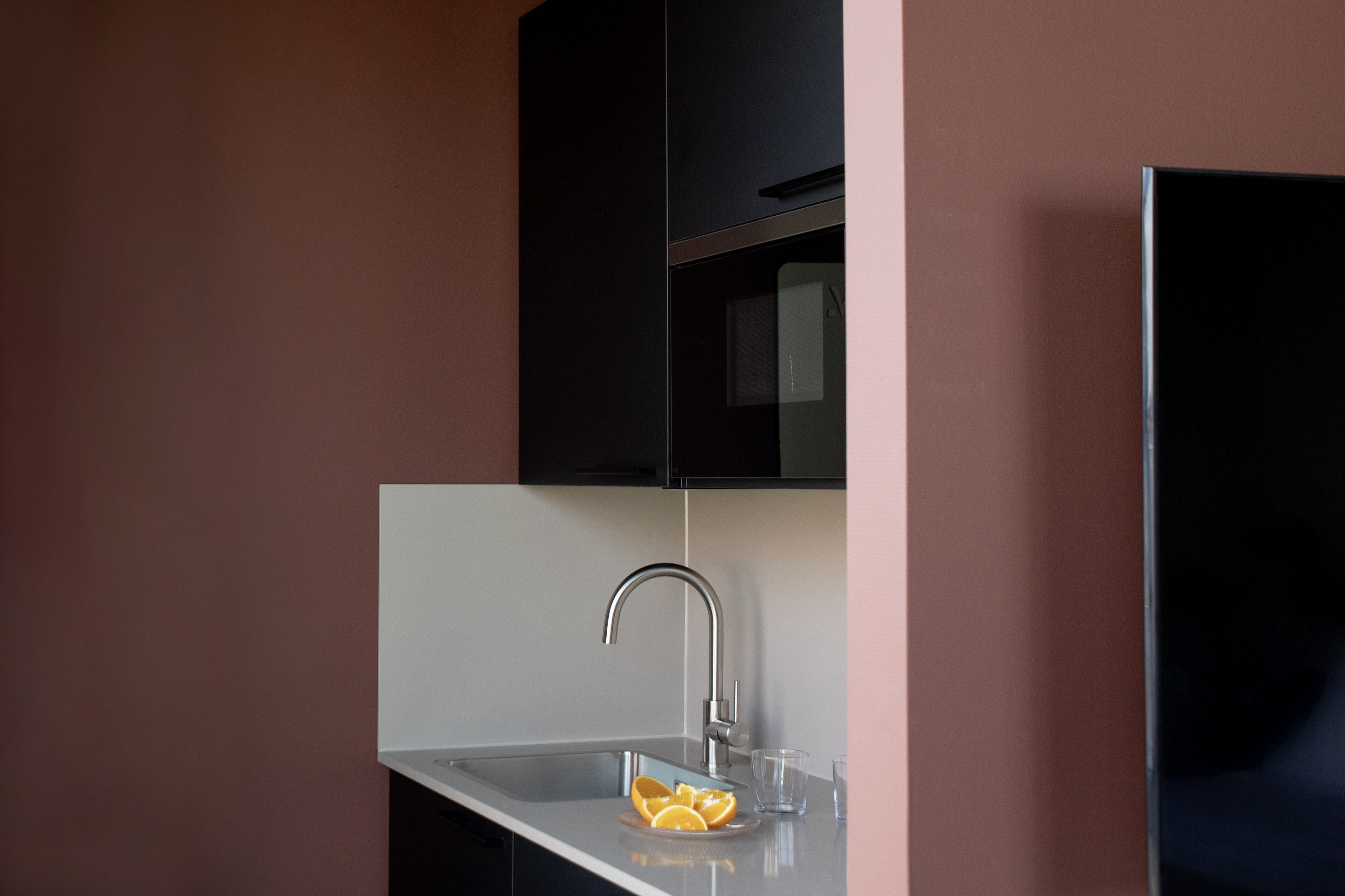 Eine moderne Küche mit Spüle aus Edelstahl, einem schwarzen Schrank darüber und einer Glasschüssel mit Orangenscheiben auf der Arbeitsplatte.