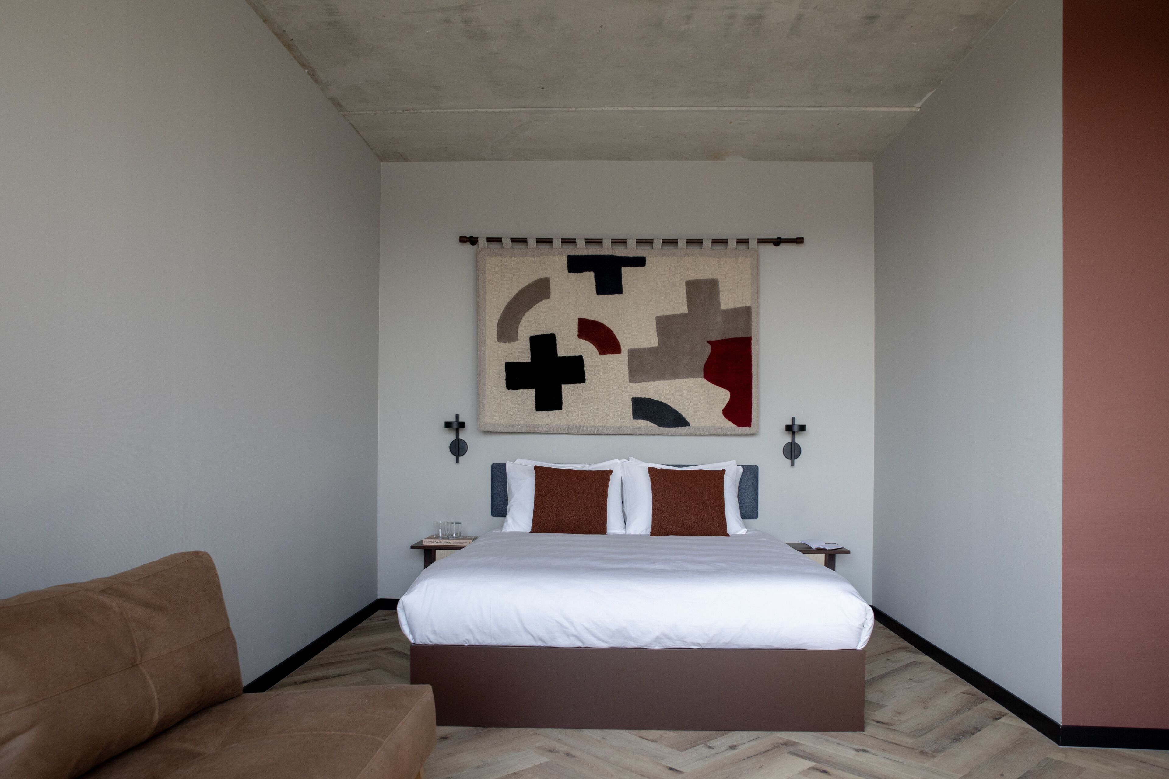 Un dormitorio moderno con una cama grande, un sofá marrón y una obra de arte abstracta colgada en la pared.
