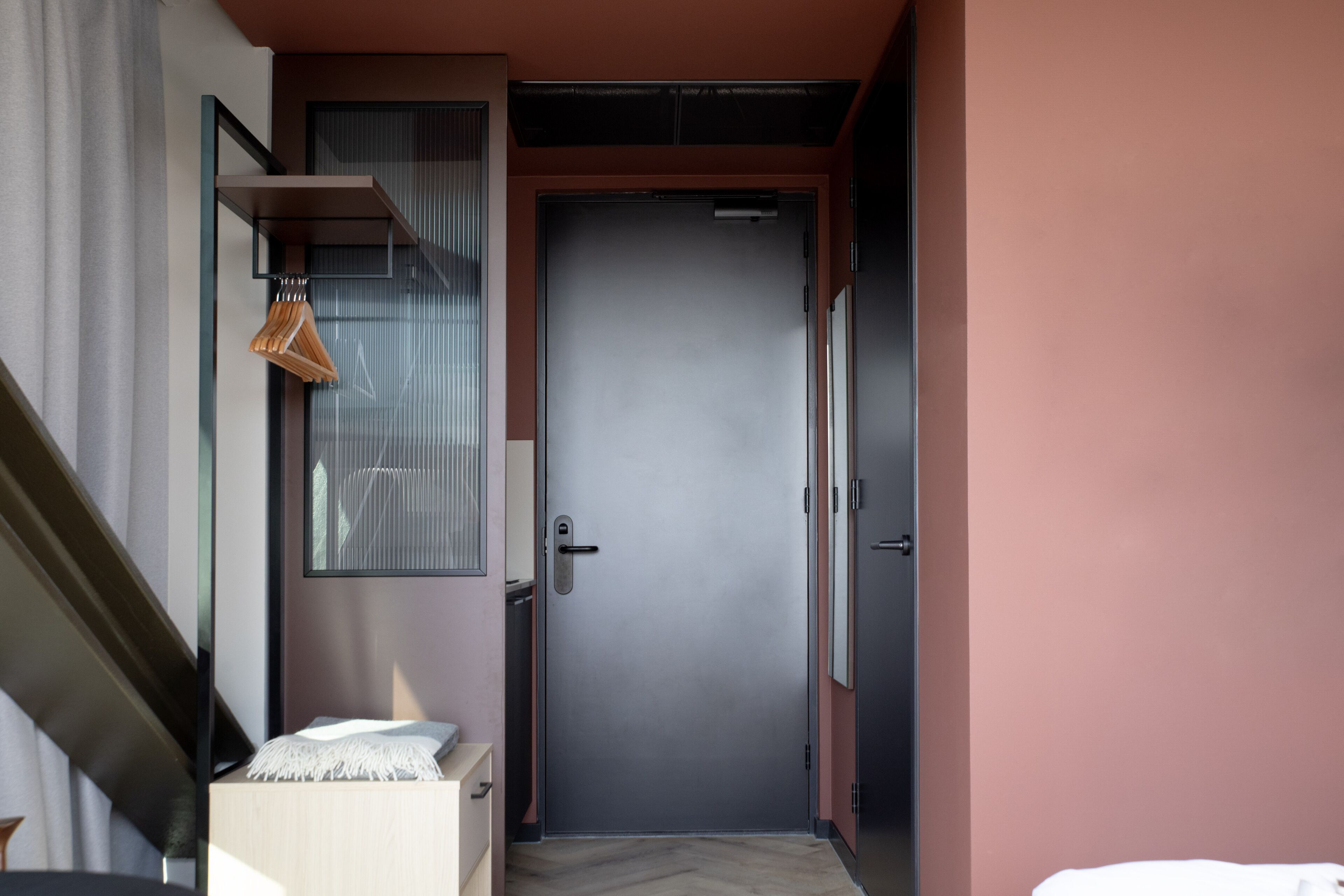 A narrow hallway leading to a door with a handle and a small shelf with clothes.