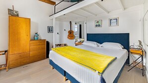 Ein Schlafzimmer mit einem Bett, einem Holzschrank, einer Gitarre und einem kleinen Tisch mit einer Lampe.