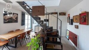 Eine moderne Küche mit einer zentralen Kochinsel, einem Essbereich mit einem langen Holztisch und einer Treppe, die zu einer oberen Ebene führt.