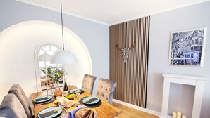 A dining area with a wooden table, chairs, and a white fireplace. - Mediterranean design apartment I Central with cathedral view (Bremen)