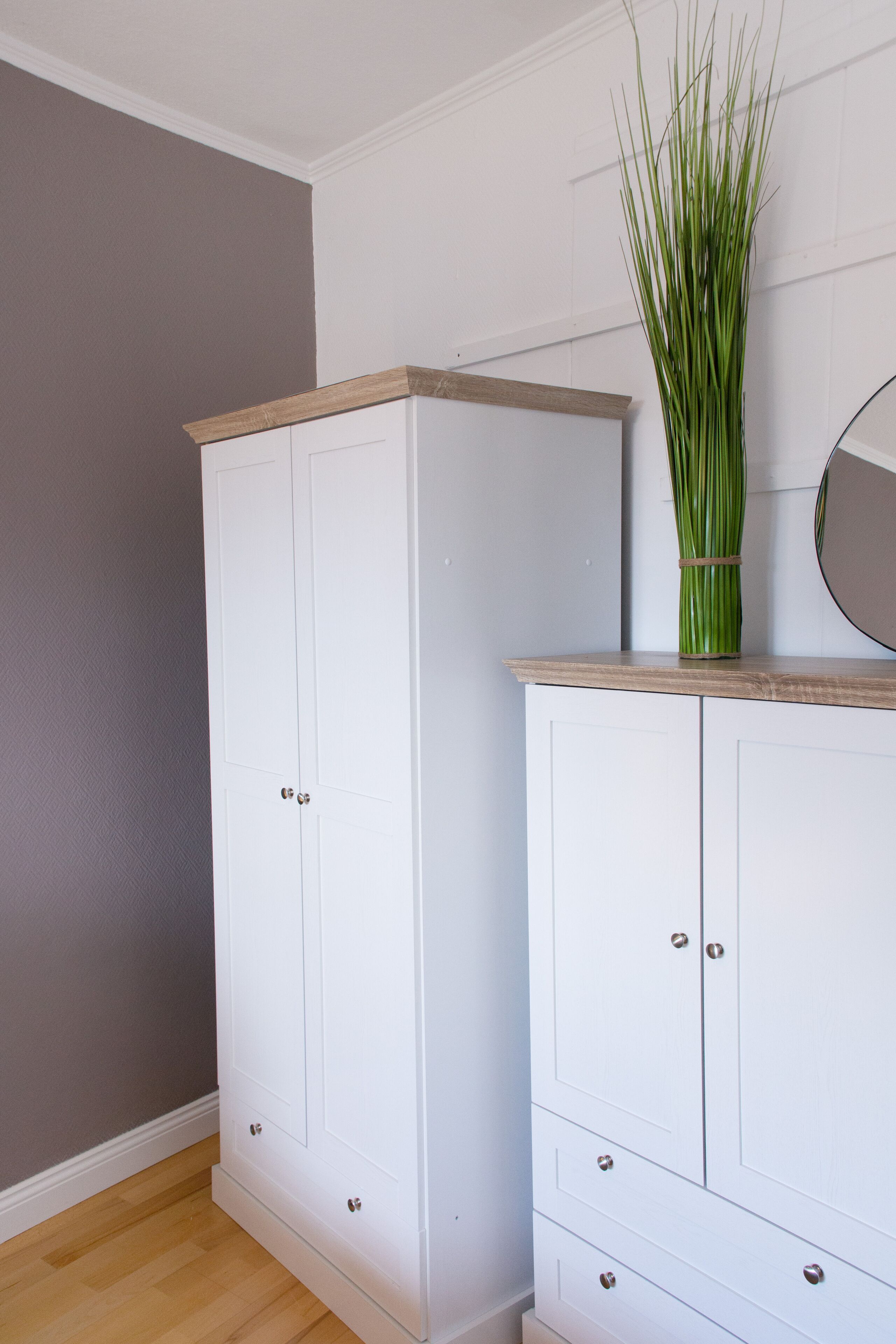 Ein weißer Kleiderschrank mit Holzauszug und einem Spiegel darüber.
