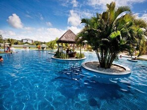 A swimming pool with multiple circular islands, palm trees, and a thatched-roof structure. - Iloa Residence (Barra de São Miguel)