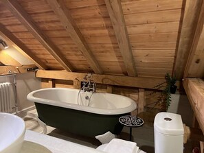 Techo de madera con una bañera, un radiador y una pequeña mesa con un adorno.