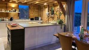 A modern kitchen with wooden beams, a central island, white cabinetry, and a dining area with a table set for two. - The Hen House (Ware)