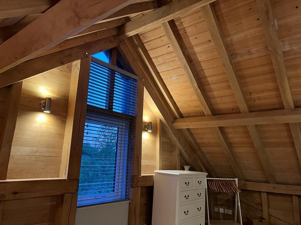 A wooden interior with a sloped ceiling, a window with blinds, and a white dresser.