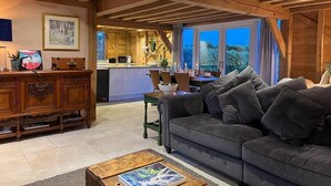 A cozy living room with a wooden ceiling, a sofa, a coffee table, and a dining area with a kitchen in the background. - The Hen House (Ware)