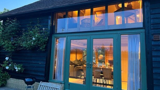 A wooden building with large glass doors and windows, a patio with outdoor furniture, and a clear view of the interior. - The Hen House (Ware)