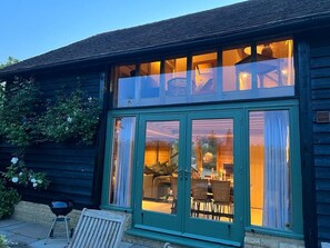A wooden building with large glass doors and windows, a patio with outdoor furniture, and a clear view of the interior. - The Hen House (Ware)