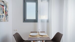 A dining area with a table set for two, a window, and a painting on the wall. - Bedspot Apartments Paros (Paros)