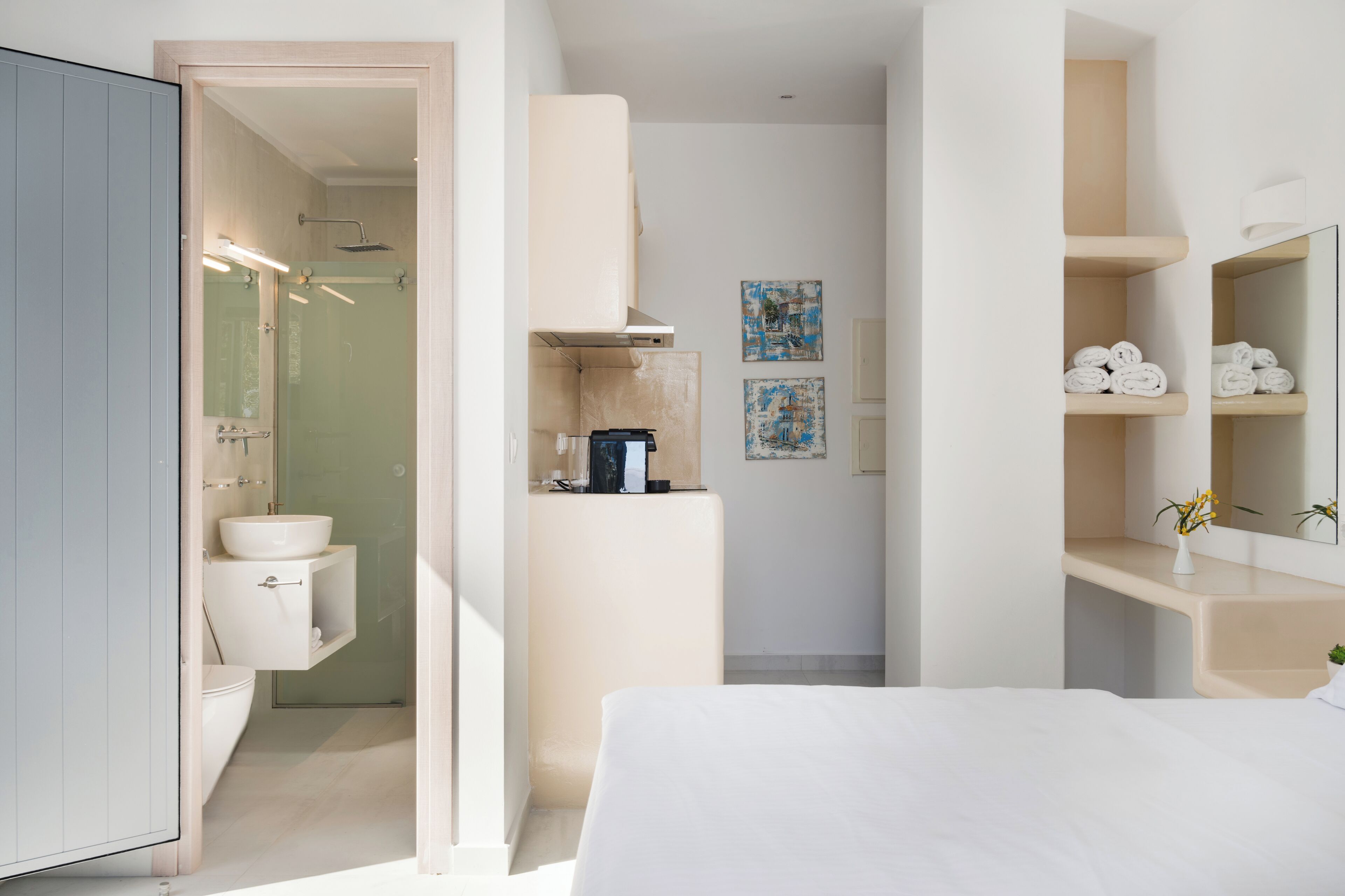 A modern hotel room with a bed, a bathroom with a shower, and a small kitchenette area.