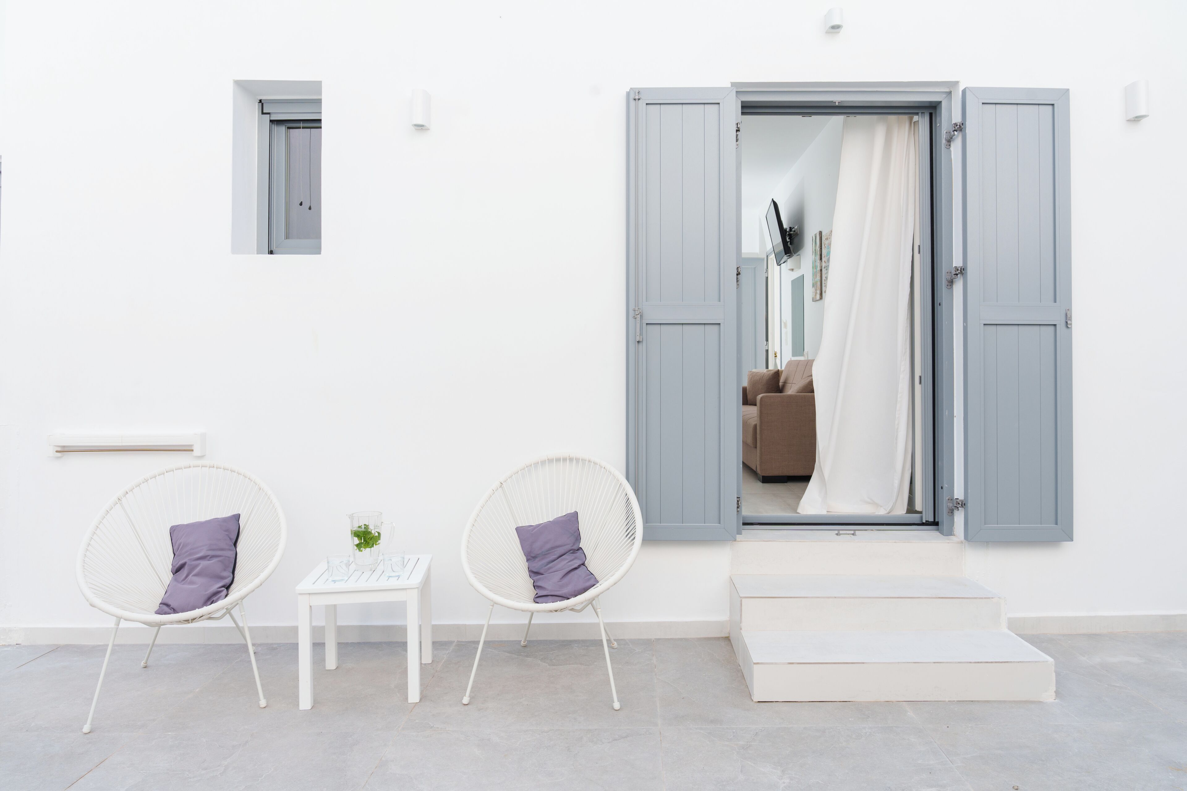 A room with two white wicker chairs with purple cushions, a small white table, and a large mirror with a blue door.