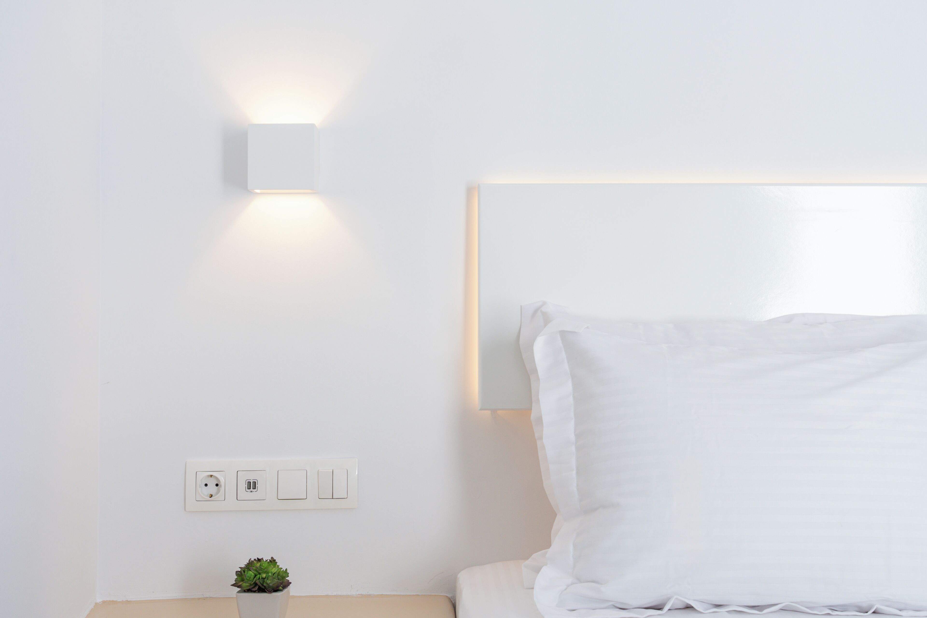 Una camera d'albergo dal design minimalista, con un letto, un comodino, una lampada a parete e una presa di corrente.
