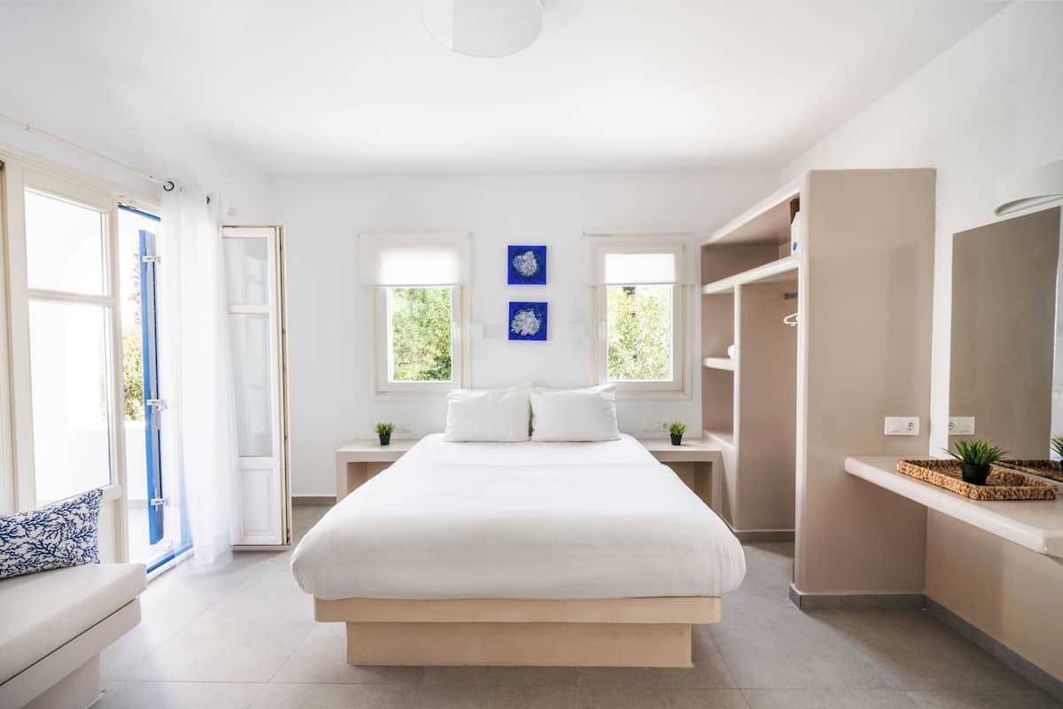 A modern bedroom with a large bed, bedside tables, a built-in wardrobe, and a window with curtains.