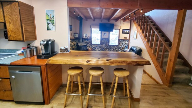 A kitchen with wooden cabinets, a coffee maker, a refrigerator, and a wooden island with stools. - Juneau Cabin near Eaglecrest & Trails (Juneau)