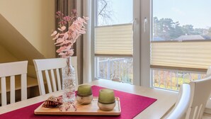 A dining table with a pink placemat, a clear glass vase with pink flowers, and two green cups on a wooden tray.