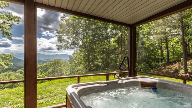 A hot tub with a wooden deck and a view of a forest and mountains. - Bear Walk-Fire Pit - Hot Tub - Charcoal Grill (Bryson City)
