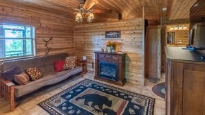 A cozy cabin interior with a wooden ceiling, a fireplace, a sofa, and a rug with a bear design. - Bear Walk-Fire Pit - Hot Tub - Charcoal Grill (Bryson City)