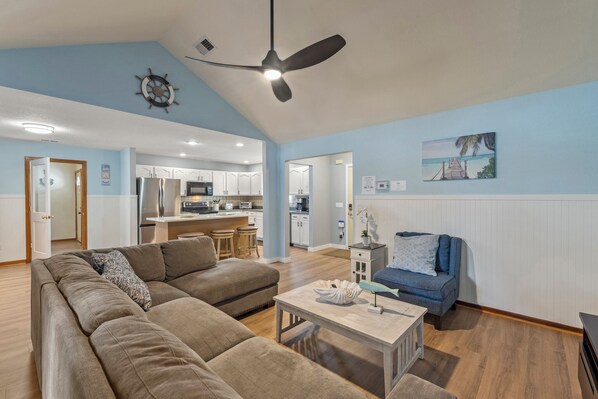 A spacious living room with a large sofa, a coffee table, and a dining area with a kitchen in the background.