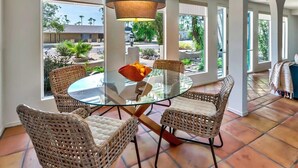 A dining area with a glass table and wicker chairs, large windows, and a view of the outside. - Spacious Desert Home | Heated Pool (Scottsdale)