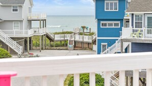 Una proprietà fronte mare con un patio in legno, una scala che conduce a un balcone e vista sull'oceano.