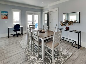 Un comedor con una mesa de madera, sillas blancas, un tapete y un jarrón con flores.