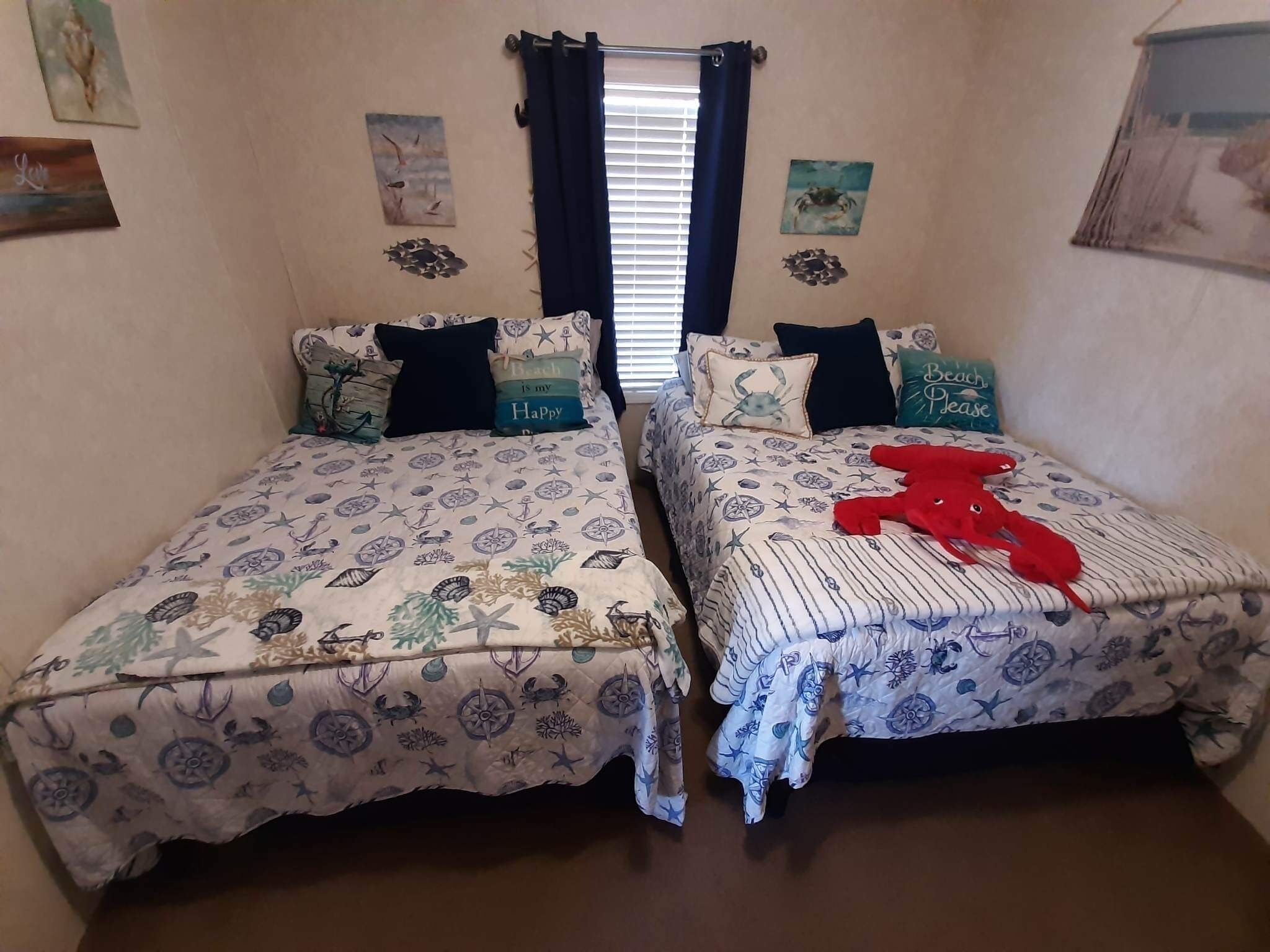 Ein Schlafzimmer mit zwei Betten, jeweils mit einem wellenschlagbezogenen Bettbezug. Es gibt dekorative Kissen, ein rotes Plüschtier auf dem rechten Bett und ein Fenster mit Vorhängen.