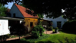 Ein zweistöckiges Haus mit rotem Dach, gelbem Anstrich und einem Garten mit Rasen und Blumentöpfen.