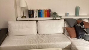 Ein modernes Wohnzimmer mit einem weißen Sofa, einem Glastisch mit Dekoration, einer Bücherwand mit Büchern und einem Gemälde an der Wand.