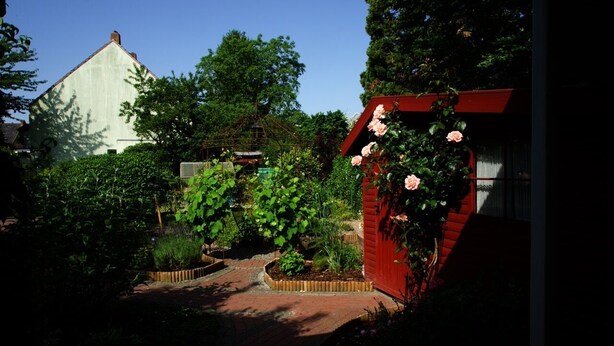 Ein Garten mit einer roten Struktur, einem weißen Gebäude und einem Holzzaun.