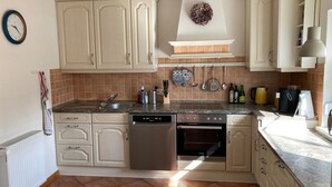 Eine Küche mit weißen Schränken, einem Geschirrspüler, einem Backofen und einem Waschbecken. An der Wand hängt eine Uhr und über den Schränken ein Kranz.