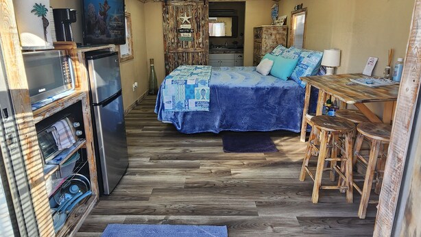 A compact RV interior with a kitchenette, a bed with a blue bedspread, a dining area with stools, and a ceiling fan. - The Sea Shed (Perry)