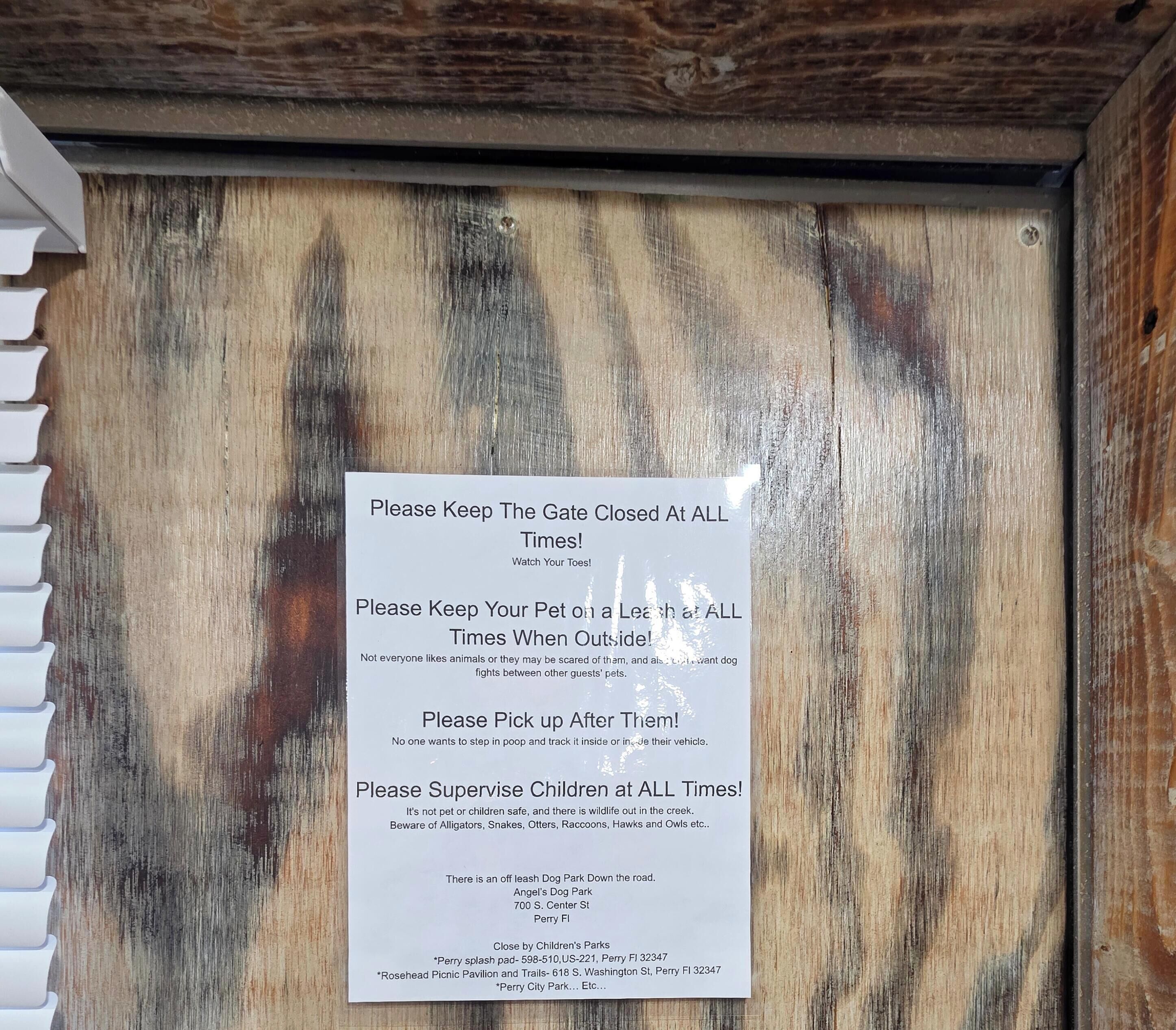A wooden door with a sign listing rules for guests, including keeping the gate closed, pets on a leash, picking up after pets, and supervising children.