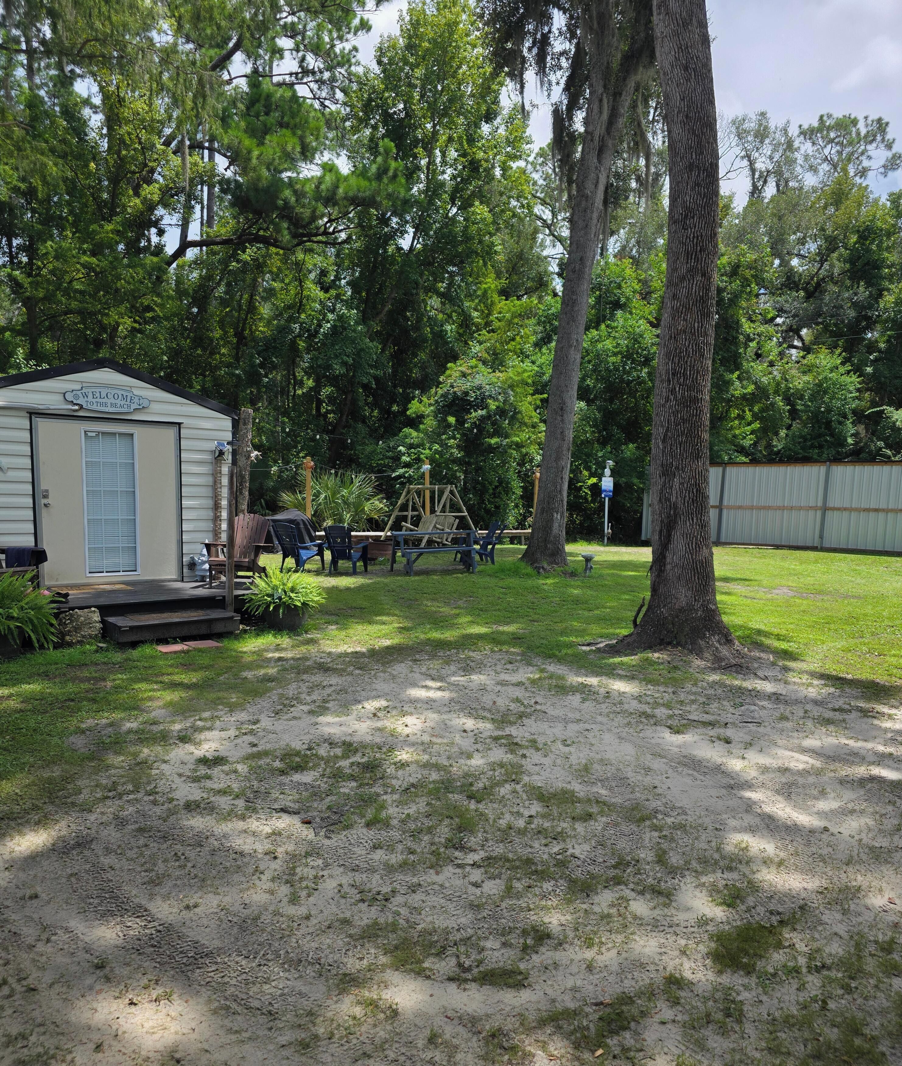 A mobile home with a porch, surrounded by trees and a fenced yard.