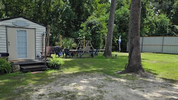 A mobile home with a porch, surrounded by trees and a fenced yard.