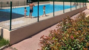 A multi-story residential building with balconies, a swimming pool, and a green fence.