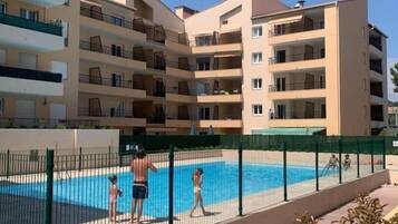 Un edificio residenziale a più piani con balconi, una piscina e un recinto verde.