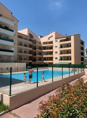 Un edificio residenziale a più piani con balconi, una piscina e un recinto verde.