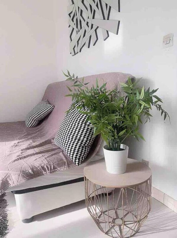 A modern living room with a sofa, patterned cushions, a potted plant, and a geometric wall art piece.