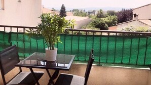 A balcony with a glass table and two chairs, a potted plant, and a green fence.