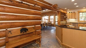 Interno di una baita in legno con una panca, un'area pranzo e una cucina con armadietti in legno e pavimento in pietra.