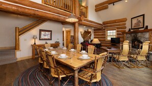 Un'ampia sala da pranzo con tavolo e sedie in legno, un caminetto e un'accogliente zona relax con poltrone Adirondack.