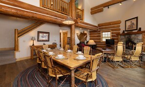 Un vaste espace dédié à la salle à manger, avec une table et des chaises en bois, une cheminée et un coin salon confortable agrémenté de fauteuils Adirondack.