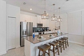 A modern kitchen with white cabinetry, stainless steel appliances, a central island with bar stools, and pendant lighting.
