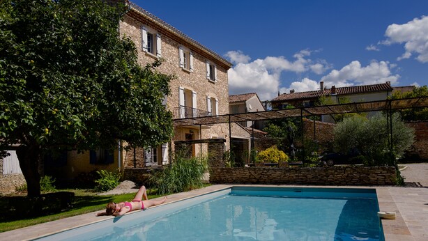 A swimming pool with a person lying on the edge, surrounded by stone buildings and greenery. - Traumhaftes Anwesen, Dorflage, am Fuße des Mt. Ventoux (Villes-sur-Auzon)