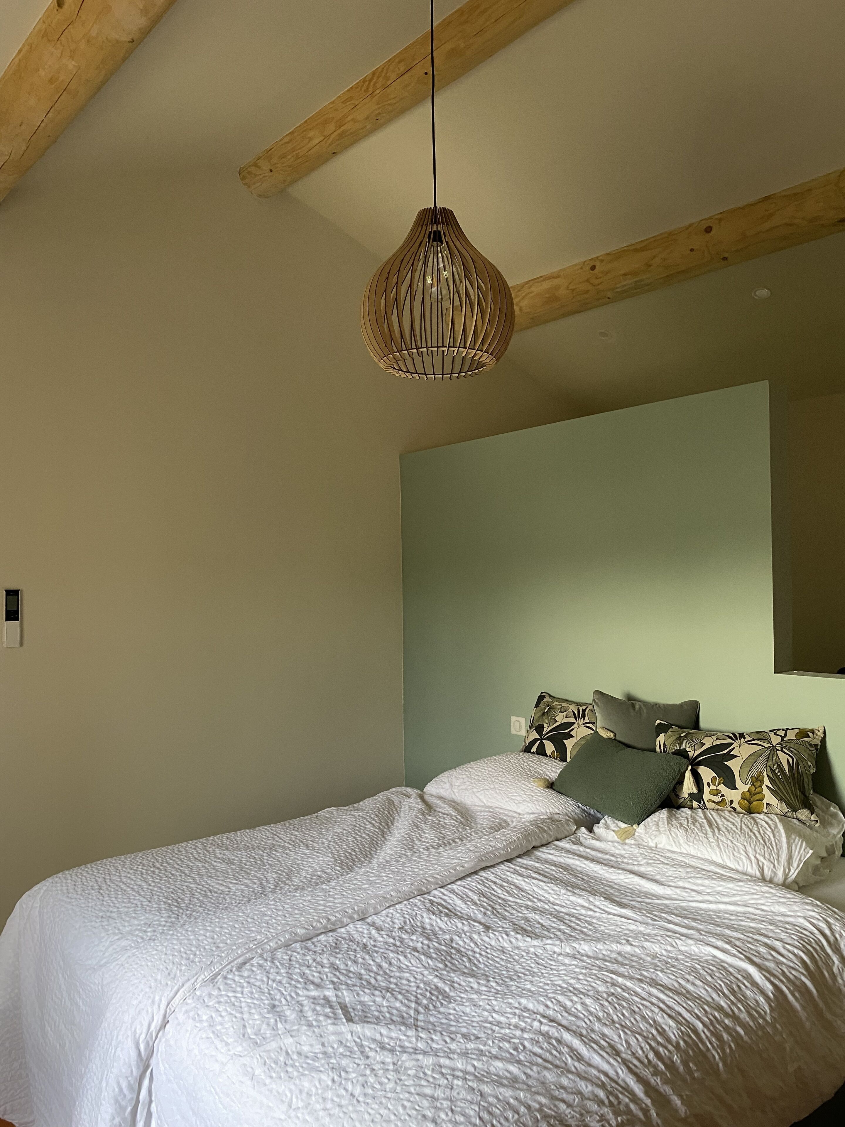 Un dormitorio con cama, lámpara colgante y viga de techo de madera.