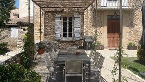 An outdoor patio with a table and chairs, a pergola overhead, stone walls, and a stone building in the background. - Traumhaftes Anwesen, Dorflage, am Fuße des Mt. Ventoux (Villes-sur-Auzon)