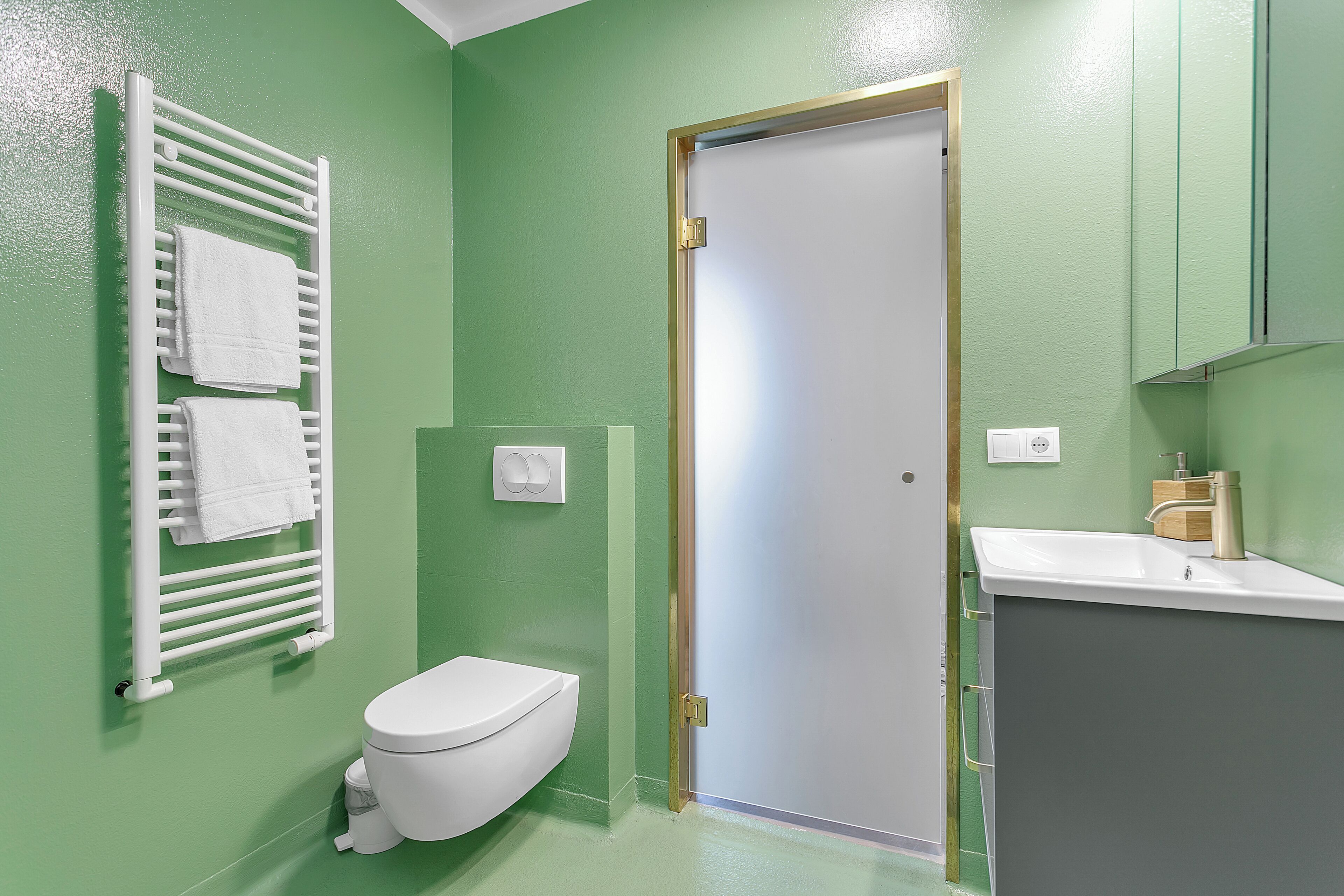 A bathroom with a white toilet, a towel rack with two towels, a sink with a faucet, and a door with a gold frame.